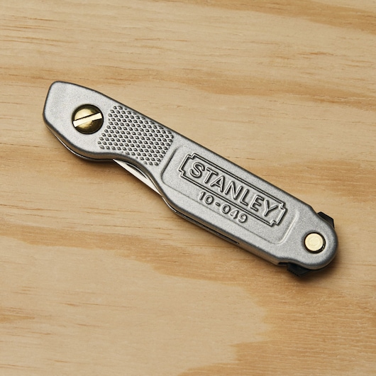 Stanley 10-049 folding utility knife with textured grip on wood surface, closed view.