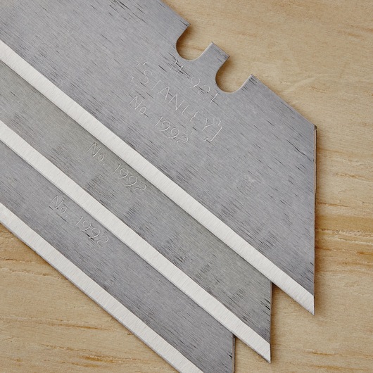 STANLEY 10-499 utility knife blades, silver color, close-up, stacked on wood surface, sharp edges visible.