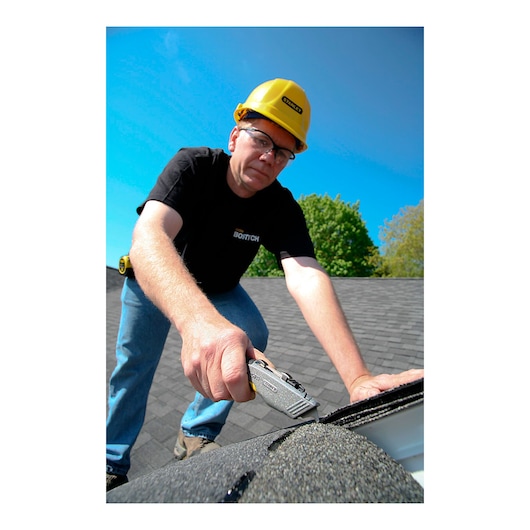 Photo of a worker using STANLEY 10-789 utility knife to cut roof shingles outdoors.