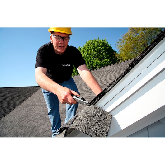 STANLEY 10-789 utility knife in use cutting roofing shingles on a house roof, outdoor setting.