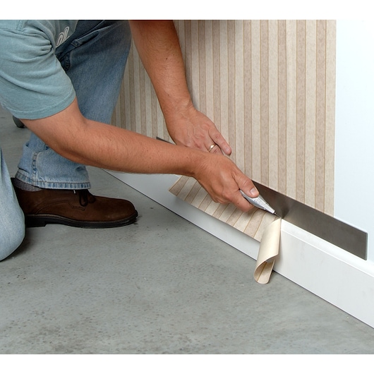 STANLEY 10-789 utility knife cutting wallpaper near floor, close-up photography.