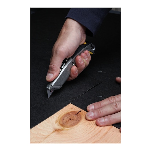 Photo of hand using STANLEY 10-789 utility knife to cut black material on wood surface.