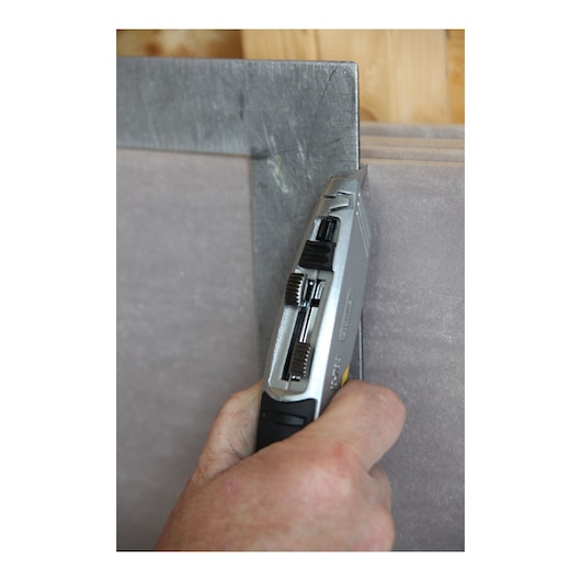 Photo of STANLEY 10-789 utility knife cutting drywall along a metal square in a construction setting.