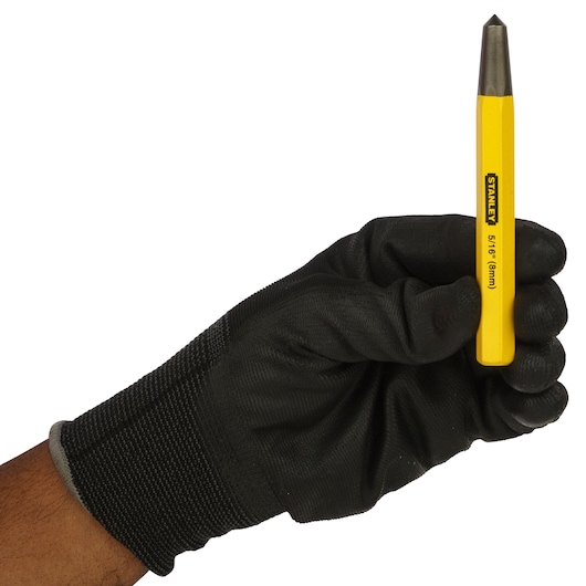 Photo of STANLEY 16-228 center punch tool held in gloved hand, yellow body, metal tip, side angle.
