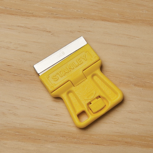 STANLEY 28-100 yellow plastic razor scraper, photography on wood surface.