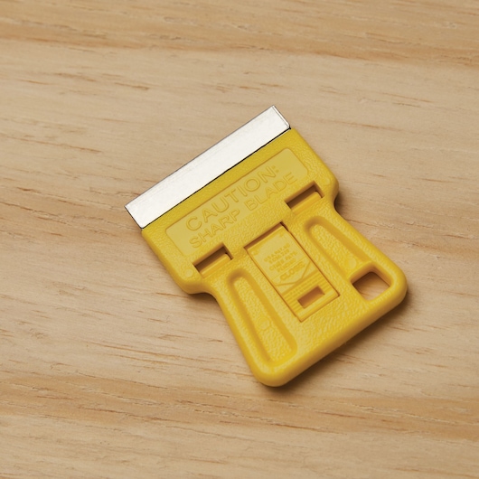 STANLEY 28-100 yellow plastic scraper with metal blade, photography on wood surface.