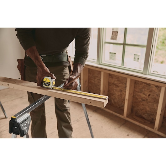 Photo of STANLEY 33-425 tape measure being used to mark a wooden board in a construction setting.