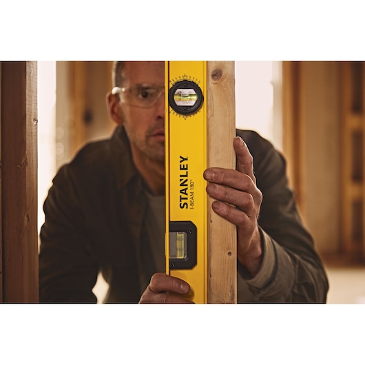 Photo of STANLEY 42-324 I-Beam 180° level tool being held against a wooden beam inside a construction site.