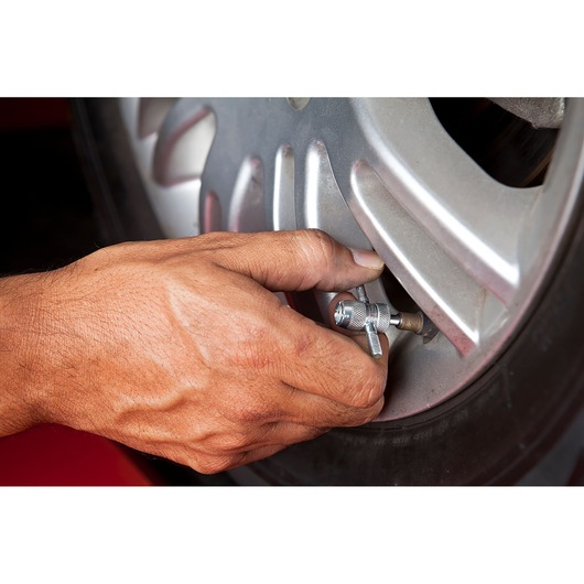 Photo of a hand using STANLEY tire valve tool, SKU 78-024, on a car wheel, close-up angle.