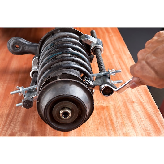 STANLEY 79-026 spring compressor tool in use on a coil spring assembly, close-up view on wooden surface.