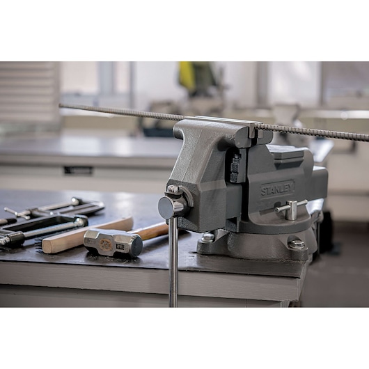 Photo of STANLEY 83-066 bench vise mounted on workbench, holding metal rod, with tools beside it.
