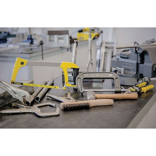 STANLEY 83-506 hand tools assortment on a workshop table, yellow hacksaw, clamps, vise, and pliers visible.