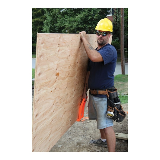 Stanley 93-301 tape measure on tool belt at construction site, side angle, with worker holding plywood.
