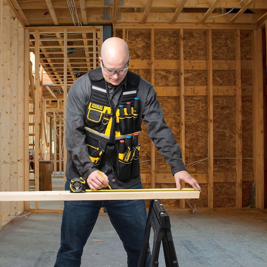 STANLEY FMST530201 tool vest with multiple pockets, worn by a person measuring wood in a construction site.