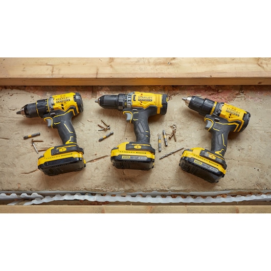 Photo of three STANLEY SBD710C2K-BR cordless drills with yellow and black casing, top view, on a work surface.