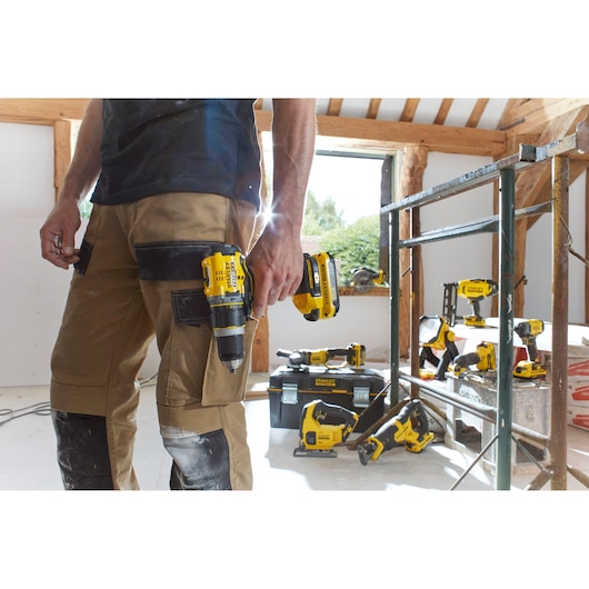 STANLEY SBD710C2K-BR drill held by worker in construction area, with STANLEY tools on ground and scaffolding.