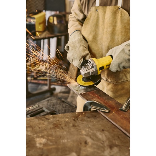 STANLEY SG7115-B3 angle grinder in use, cutting metal with sparks, close-up workshop photography.