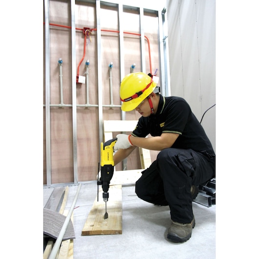 STANLEY SHR263K-BR rotary hammer drill in use on wood, worker wearing yellow hard hat and black uniform.