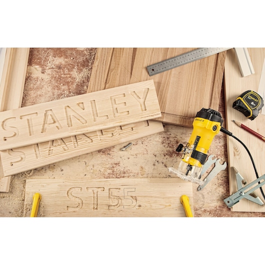 STANLEY ST55-KR woodworking router with engraved wood boards, tape measure and tools, top angle photo.