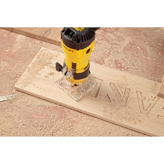 STANLEY ST55-KR router carving letters into wood on dusty workbench, close-up top view.