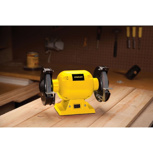 Stanley STGB3715 bench grinder in yellow on a wooden workbench in a workshop.
