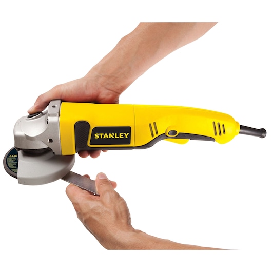 Photo of STANLEY STGS1011 angle grinder in yellow, held by hands, showing side view on white background.
