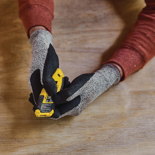 Photo of gloved hands holding a STANLEY STHT10432 utility knife on a wood surface.