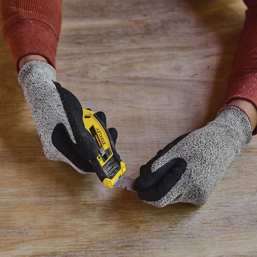 Photo of STANLEY STHT10432 utility knife with yellow and black handle, being held by gloved hands on a wooden surface.