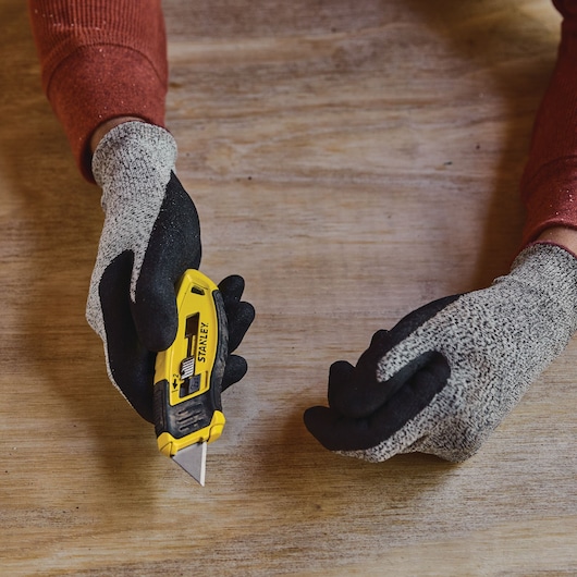 STANLEY STHT10432 utility knife held in gloved hand on wooden surface, blade extended.