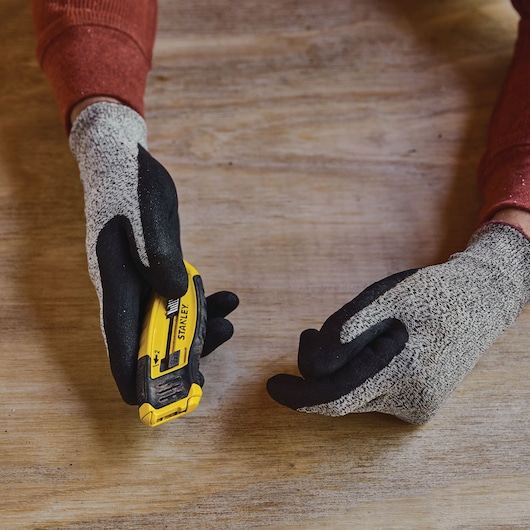Photo of STANLEY STHT10432 utility knife held in gloved hands on a wooden surface.
