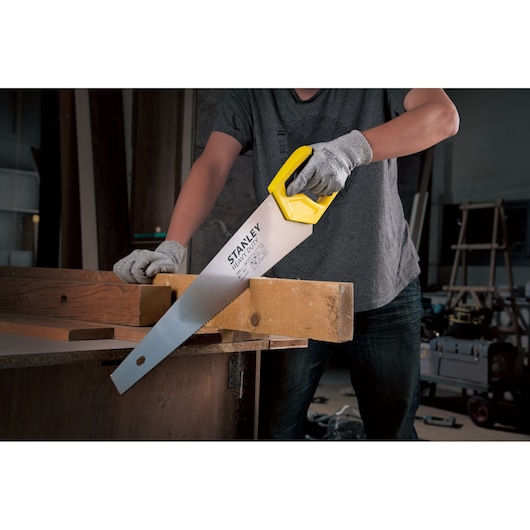 Photo of STANLEY STHT20375-LA hand saw with yellow handle cutting wood, used by a person wearing gloves.