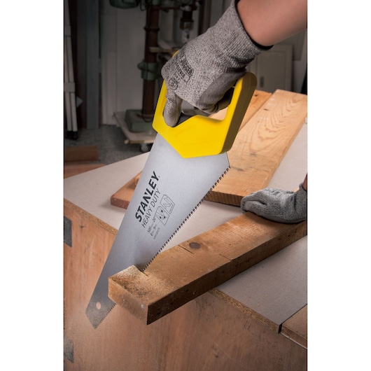 STANLEY STHT20375-LA hand saw with yellow handle cutting wood, close-up, workshop setting.