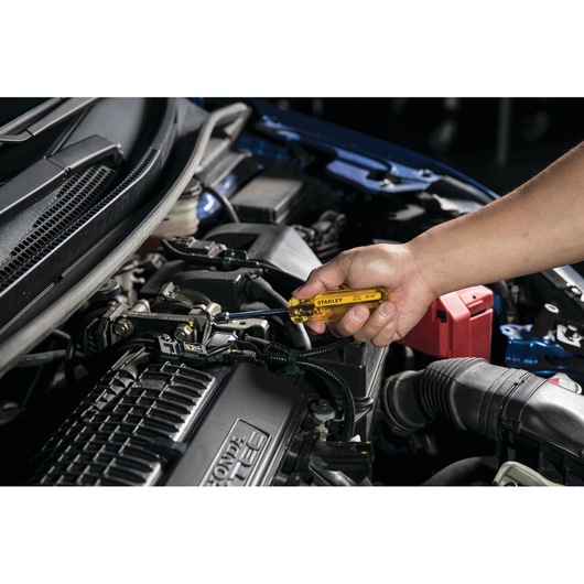 Photo of STANLEY STHT69184 screwdriver in use on car engine, close-up of hand gripping yellow handle.