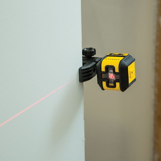STANLEY STHT77498 laser level attached to wall, projecting red horizontal line, close-up side view.
