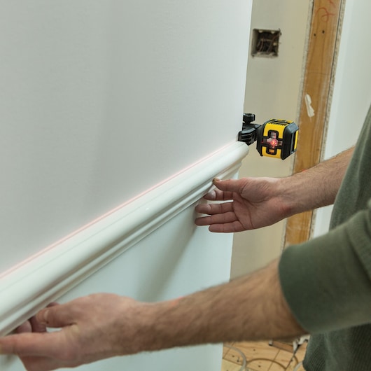 STANLEY STHT77498 laser level used to align white trim on interior wall, close-up photography.