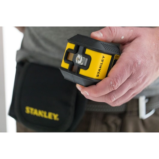 Photo of STANLEY STHT77498 yellow and black laser level held in hand, tool pouch visible in background.