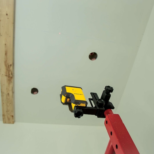 Photo of STANLEY STHT77503 laser level mounted on red pole, aimed at ceiling with drilled holes.