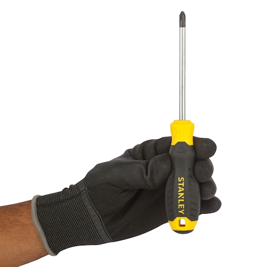 A person wearing a black work glove holds a Stanley branded Phillips screwdriver with a yellow and black handle.