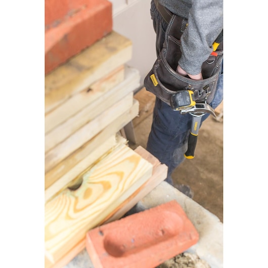 STANLEY STST1-80114 tool belt on person’s waist with hammer, close-up, construction site background.