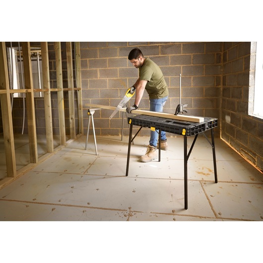 Photo of STANLEY STST11552 workbench in use with wood plank and saw in a construction setting.